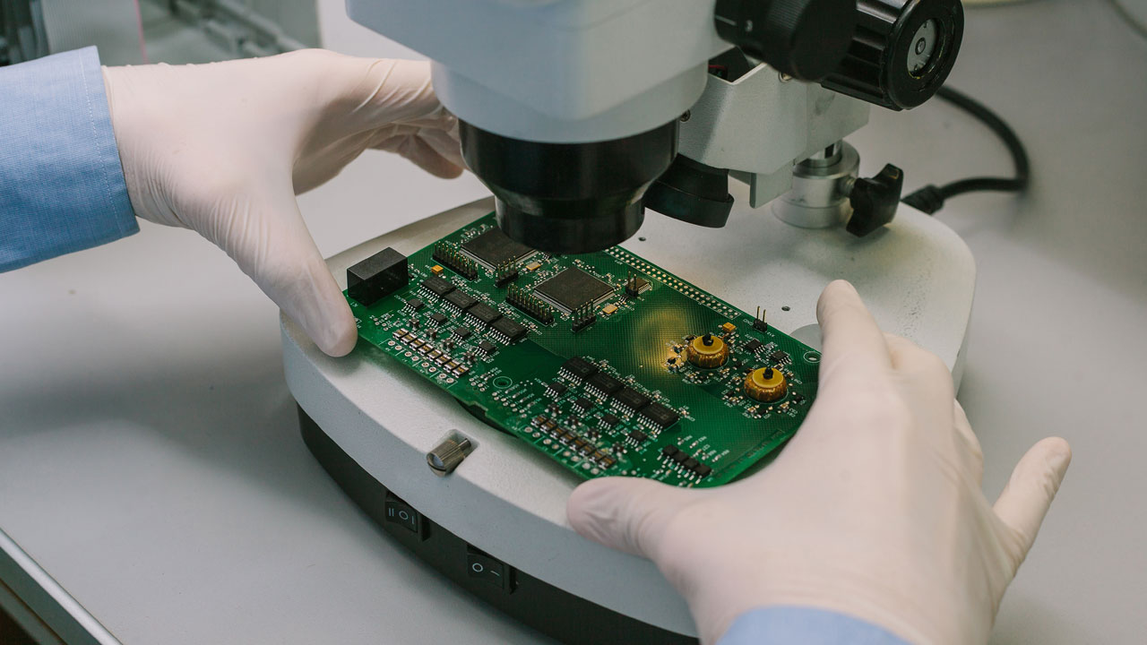 Technician performing microscopic inspection of industrial PCB for quality assurance and reliability in automation systems
