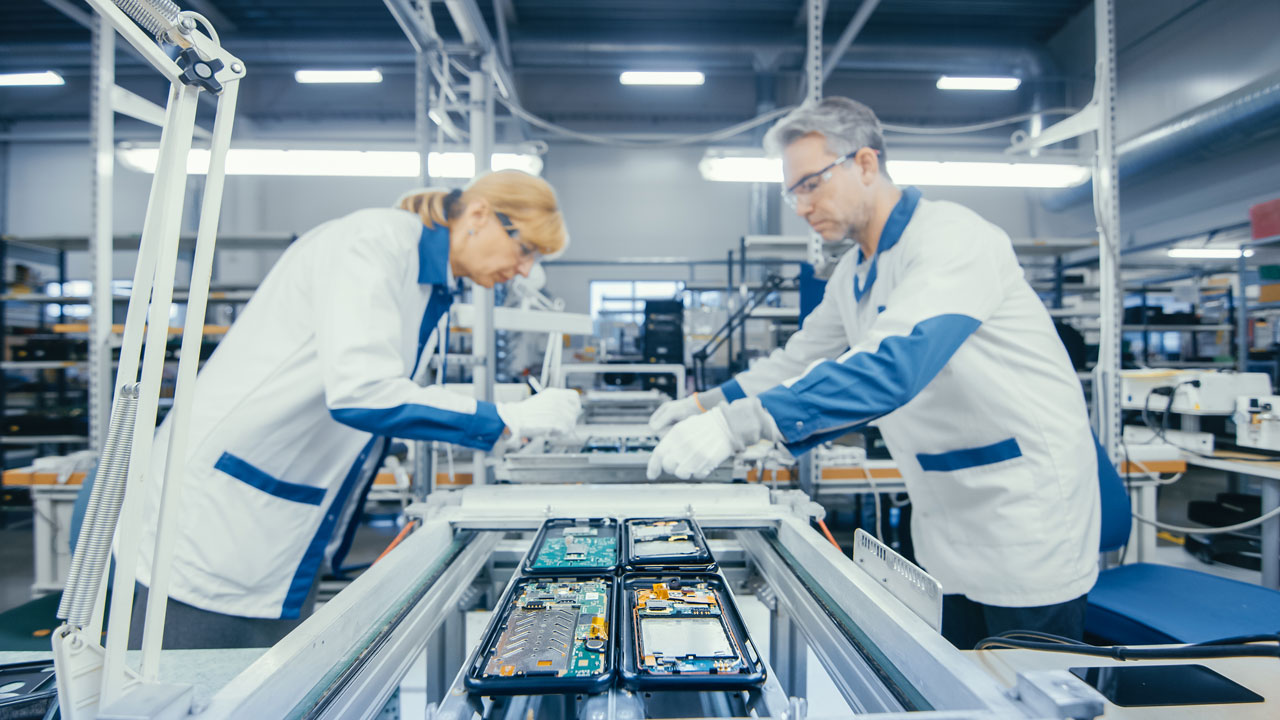Two technicians collaborating on PCB assembly in aerospace and defense factory for mission-critical builds