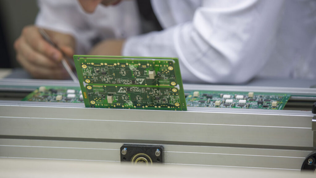 Technician inspecting PCBs on automated assembly line for emerging technology electronics with precision and reliability