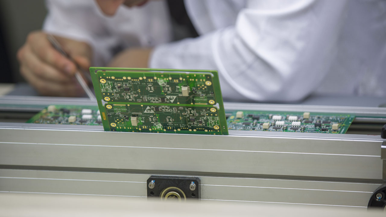 Technician inspecting PCBs on automated assembly line for emerging technology electronics with precision and reliability