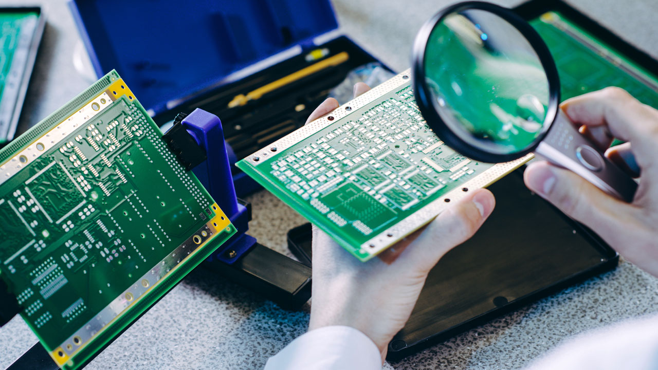 Technician inspecting PCB with magnifying glass for precision quality assurance in emerging technology electronics