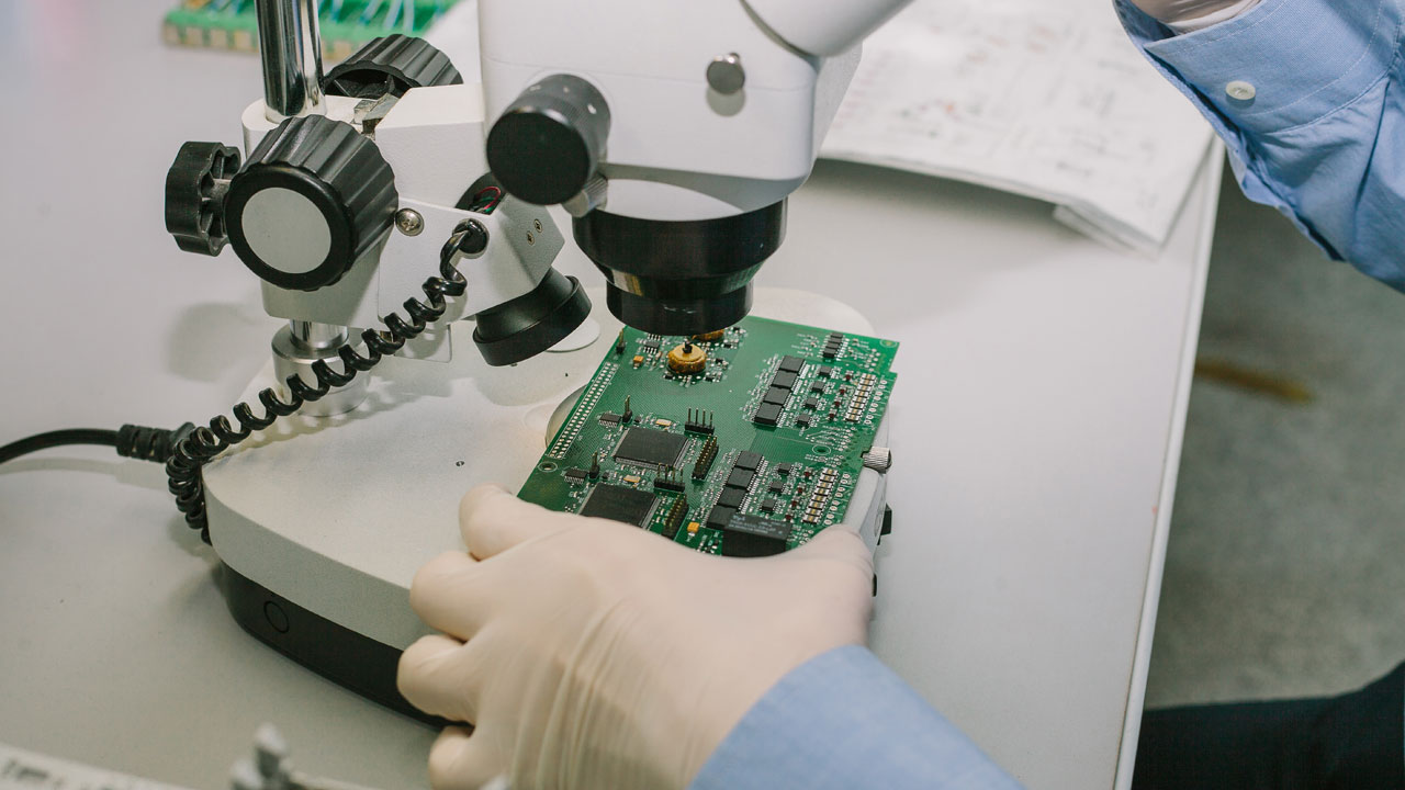 Technician inspecting telecom PCB under microscope for precision, signal integrity, and quality assurance in communications electronics