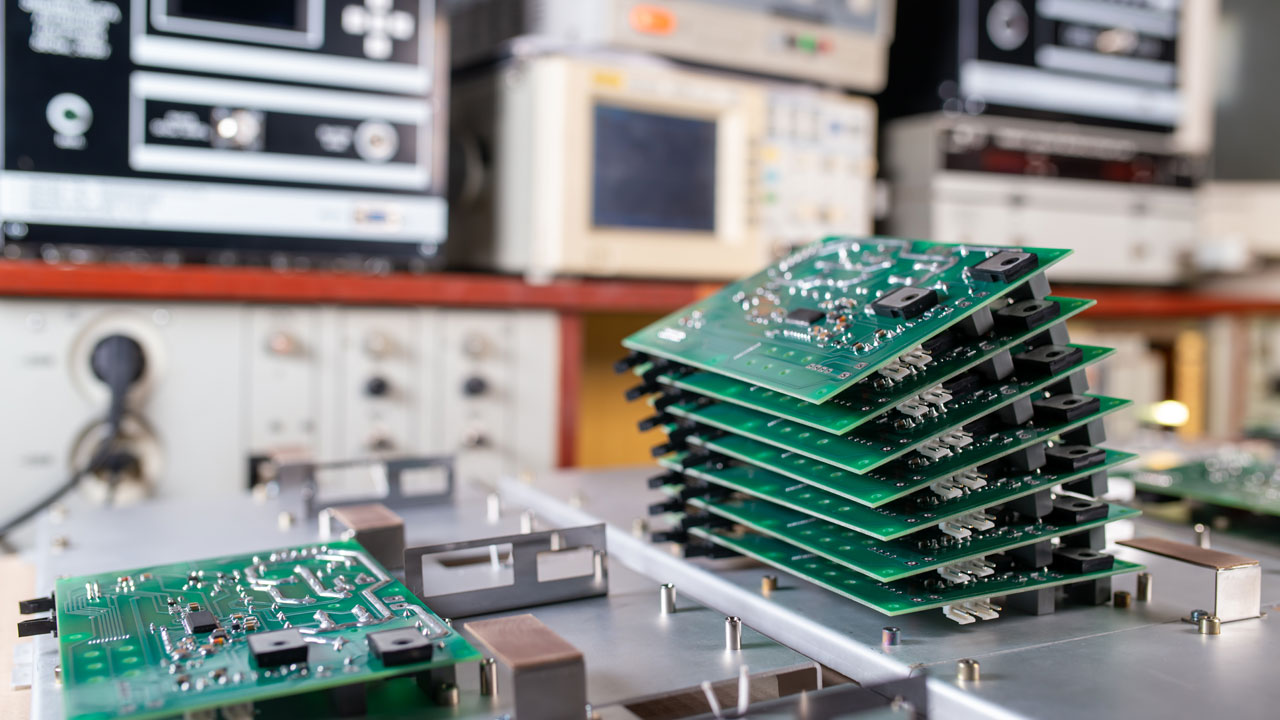 Stack of commercial PCBs in electronics lab with testing equipment for performance validation and scalable production