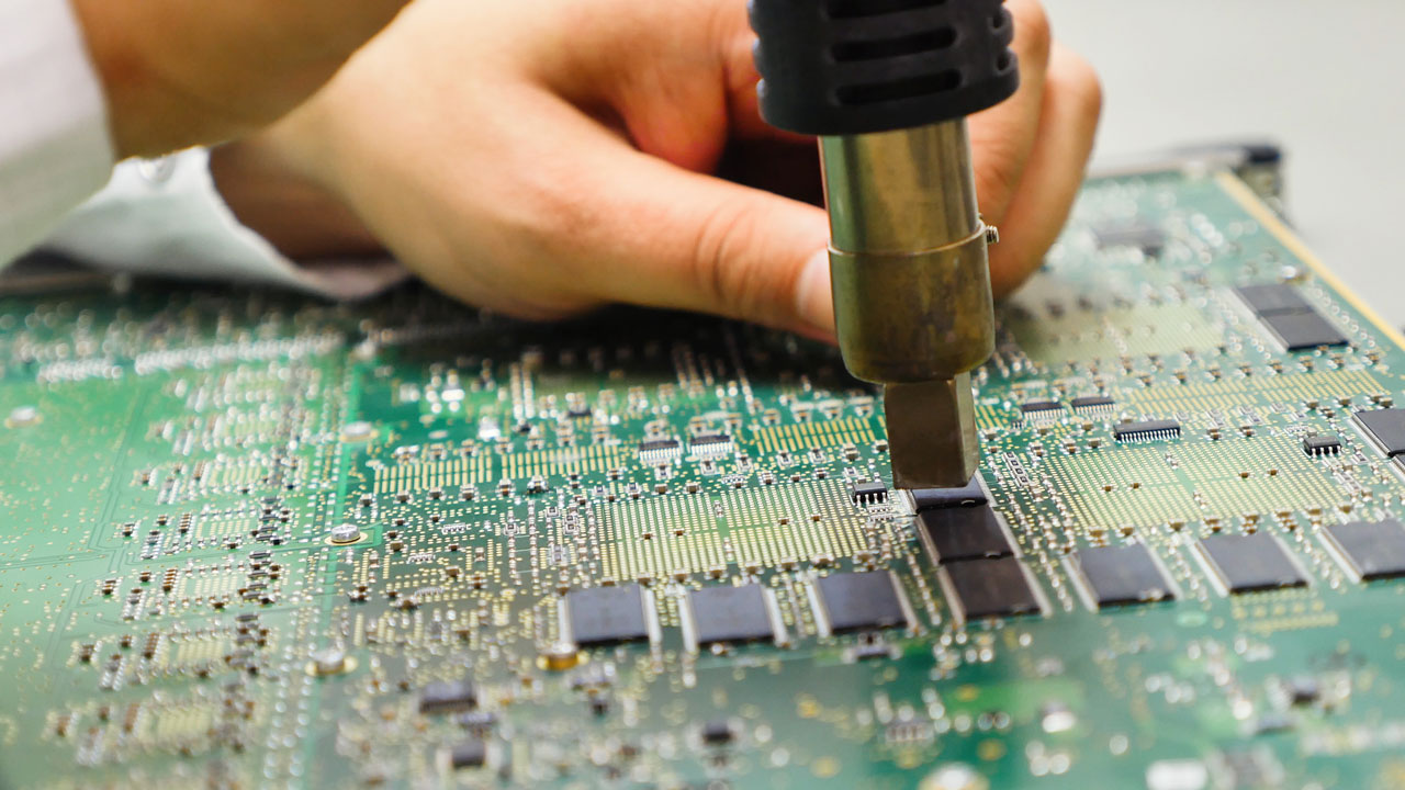 Technician performing precision rework on RF PCB using heat gun for telecom and networking electronics
