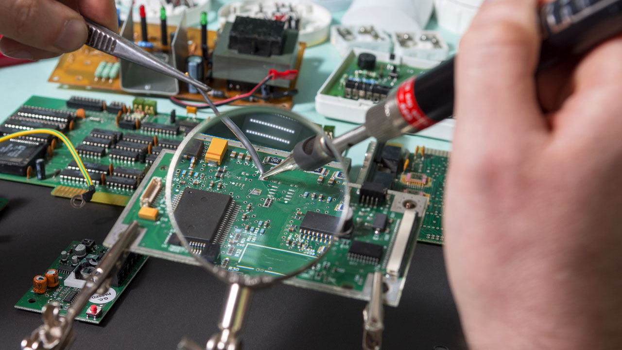 Technician performing SMT soldering on a medical PCB using magnifying glass for precision and reliability in electronics assembly