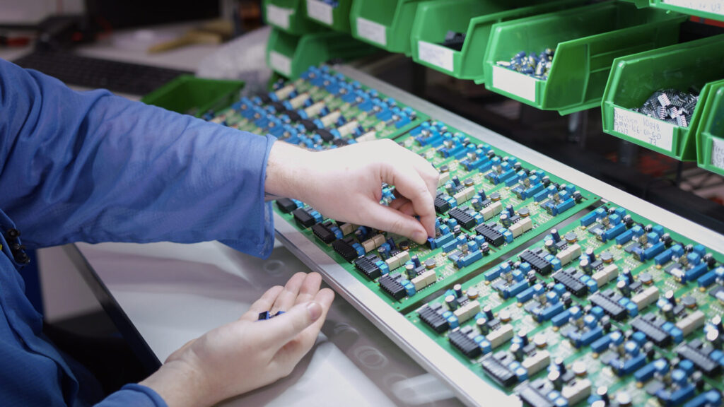 A worker inserting through-hole components on a printed circuit board assembly (PCBA) at Foxtronics EMS.