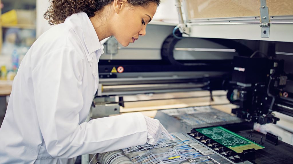 Quality control technician inspecting a mixed technology PCB assembly at a Foxtronics EMS facility.